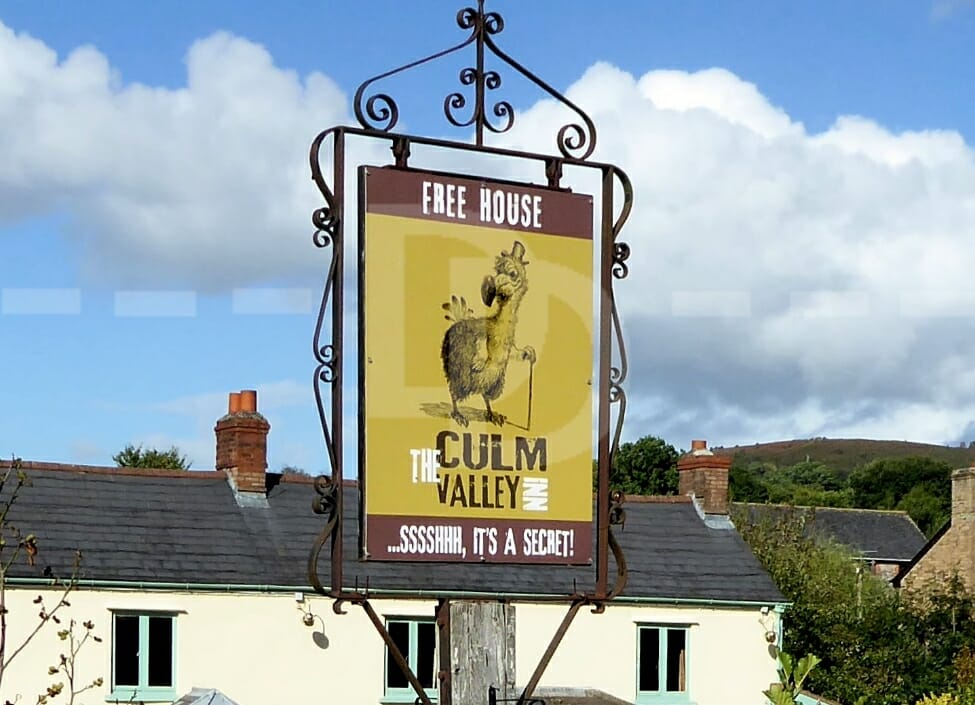 Culm Valley Inn Tiverton sign with cream building, trees and hill in the background